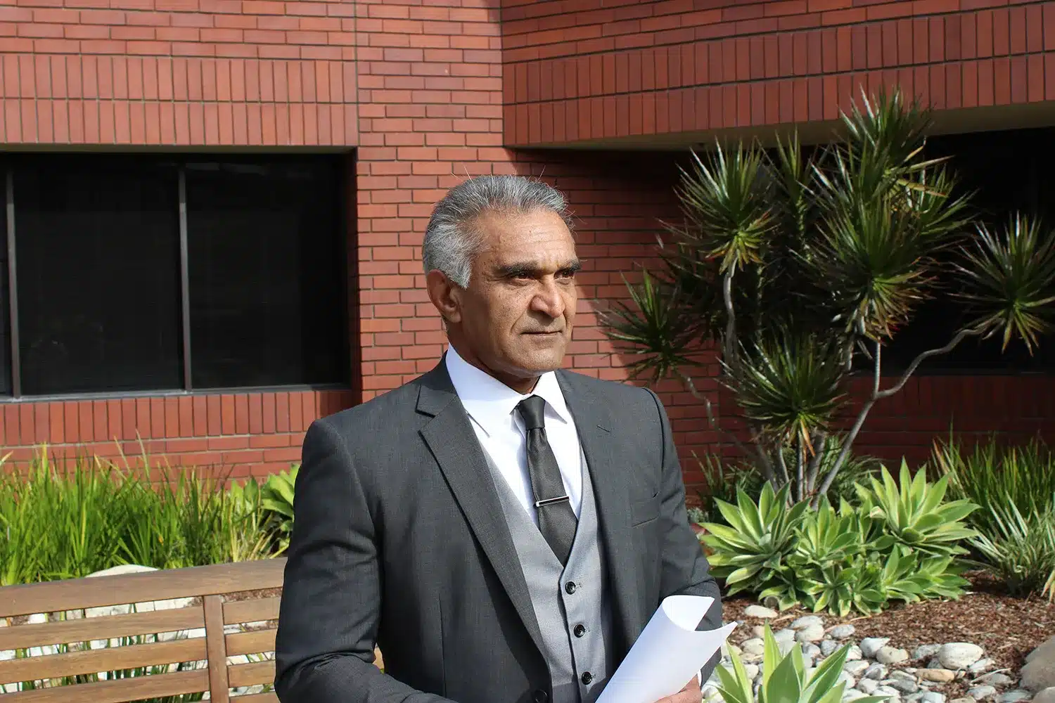 Brad Dhesi in a suit standing outside a modern California commercial building, looking at project documents.