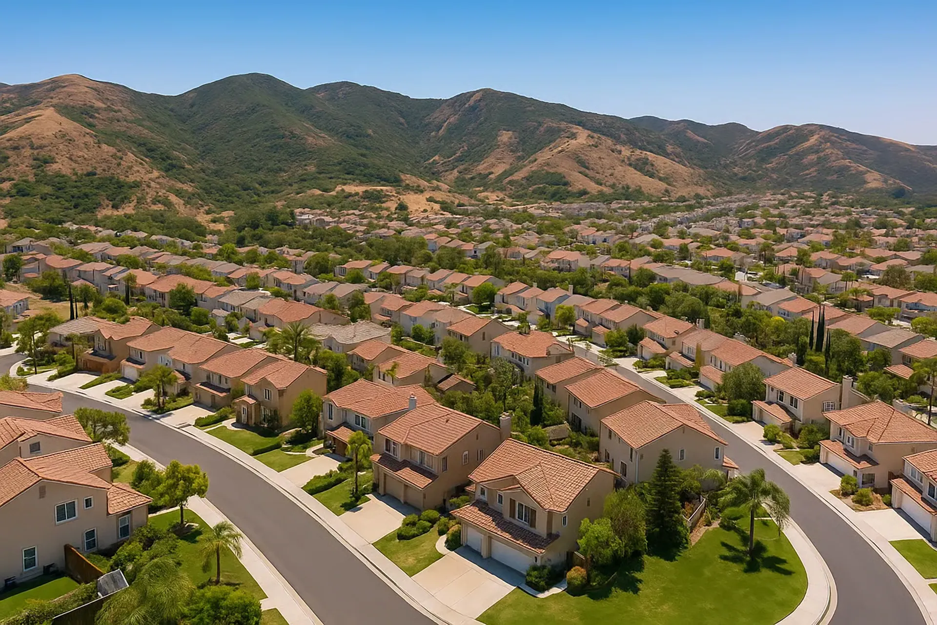 High aerial view of a Foothill Ranch, California neighborhood with two-story houses, red roofs, and neat yards by the mountains.
