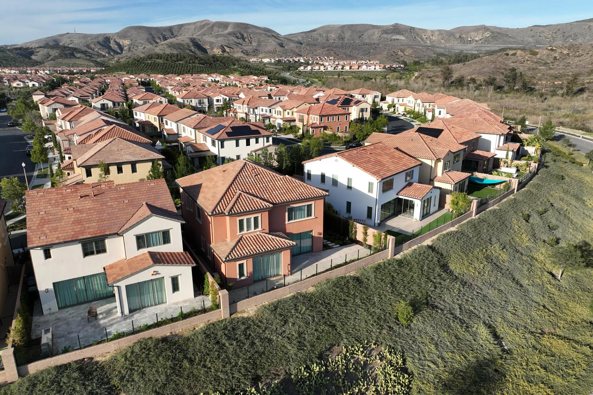 High aerial view of a luxury neighborhood in Irvine, California, with two-story houses, red roofs, solar panels, and green open spaces.