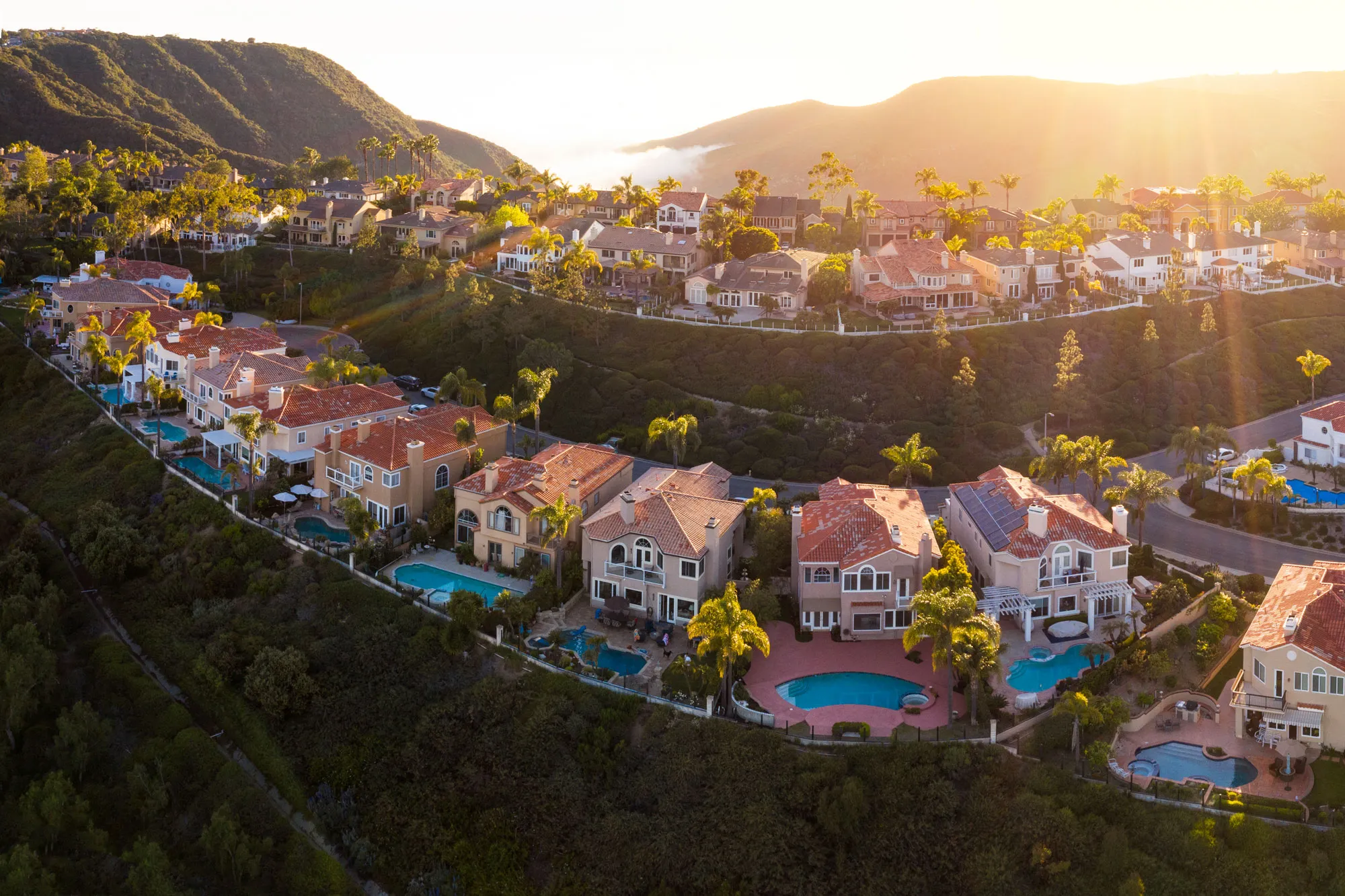Aerial view of hilltop houses in Laguna Niguel, California, with Mediterranean-style homes, pools, and a valley below.